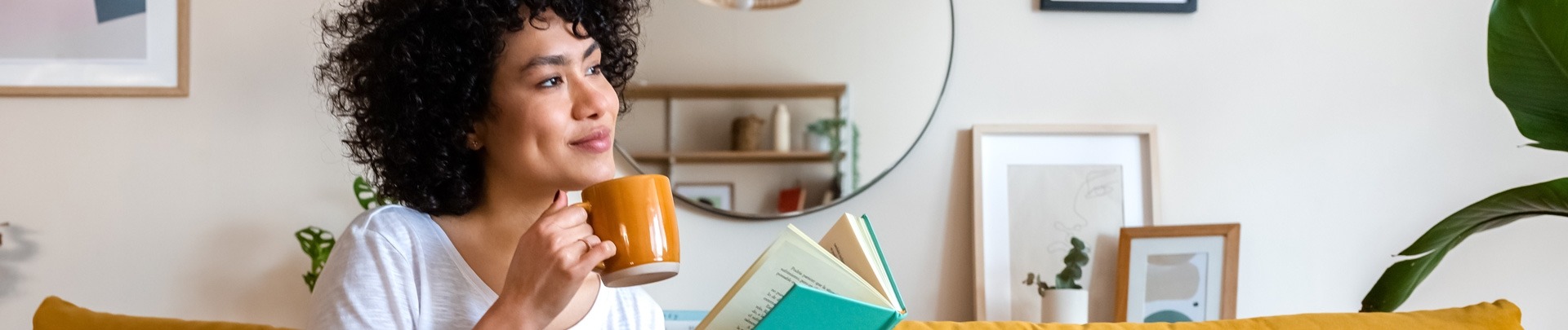 Een ontspannen Afro-Amerikaanse vrouw leest thuis een boek en drinkt koffie op de bank